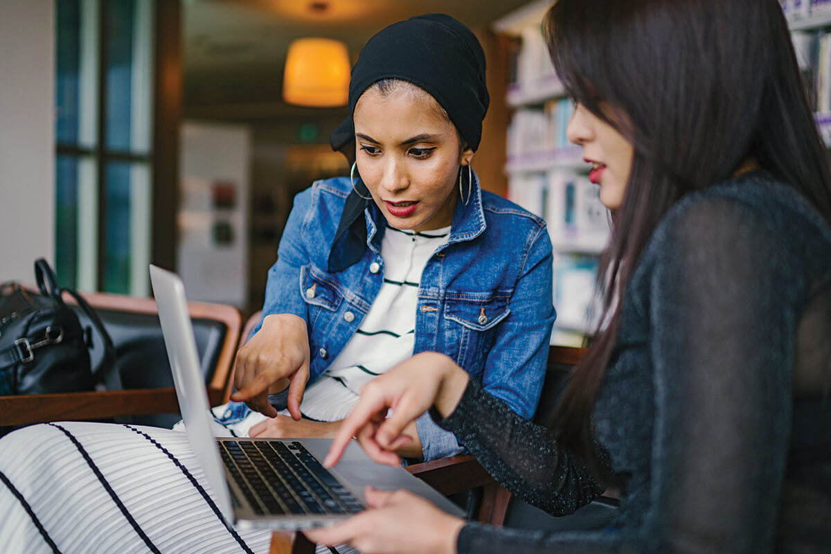 Two women working together on a laptop in the library